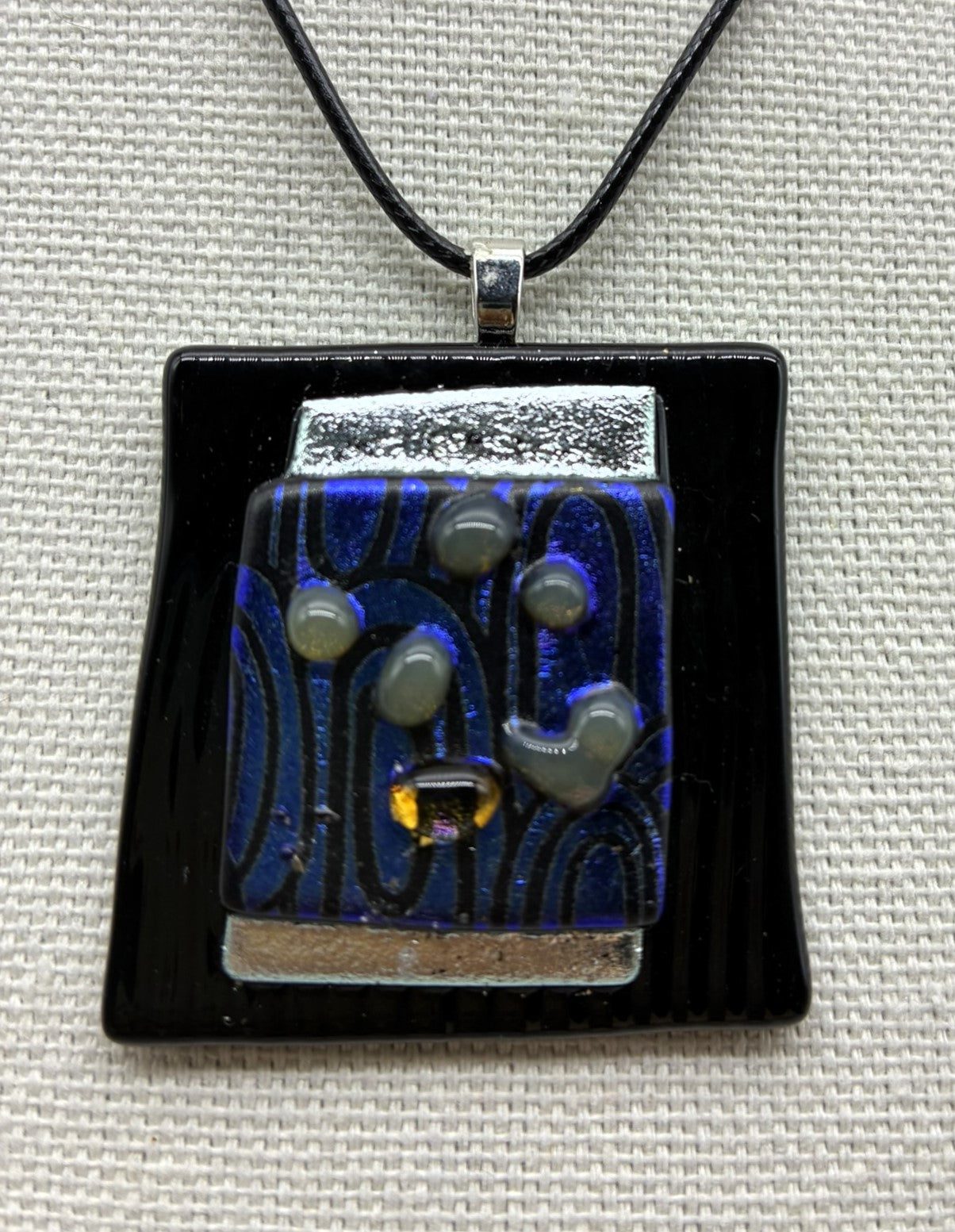 Jewelry -Offset square of black raised glass with dichroic silver and blue and black swirl glass.